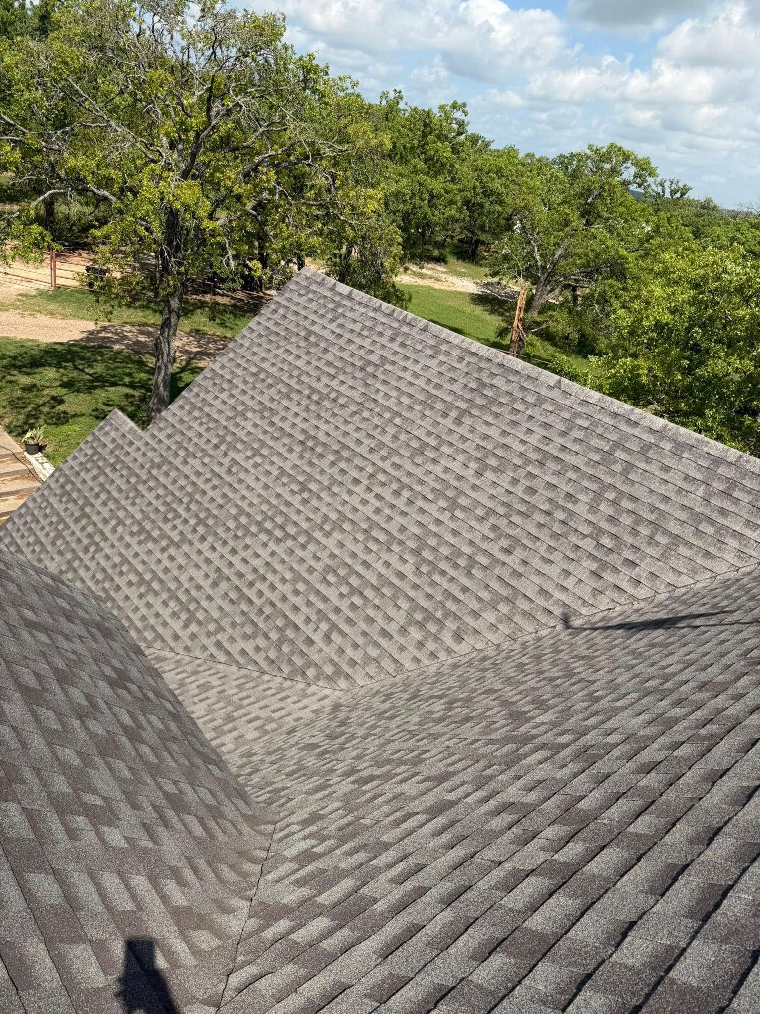 Gray shingled rooftop with trees and blue sky in the background