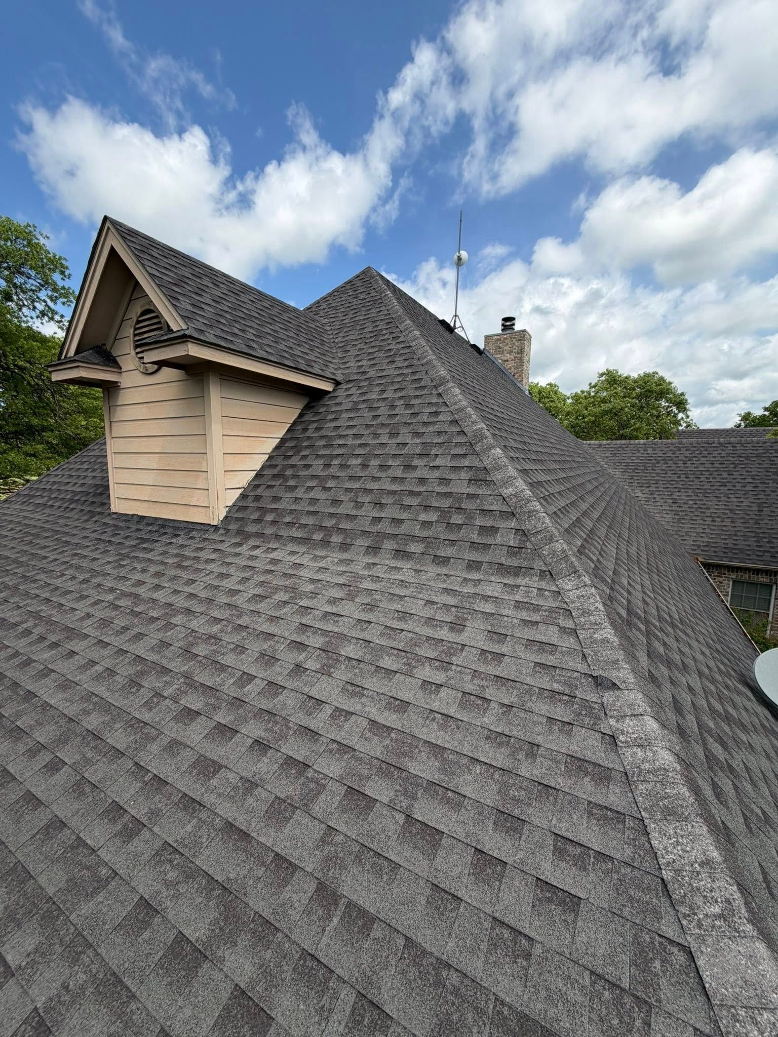 Gray shingled roof with steep peaks and a small dormer under a cloudy sky