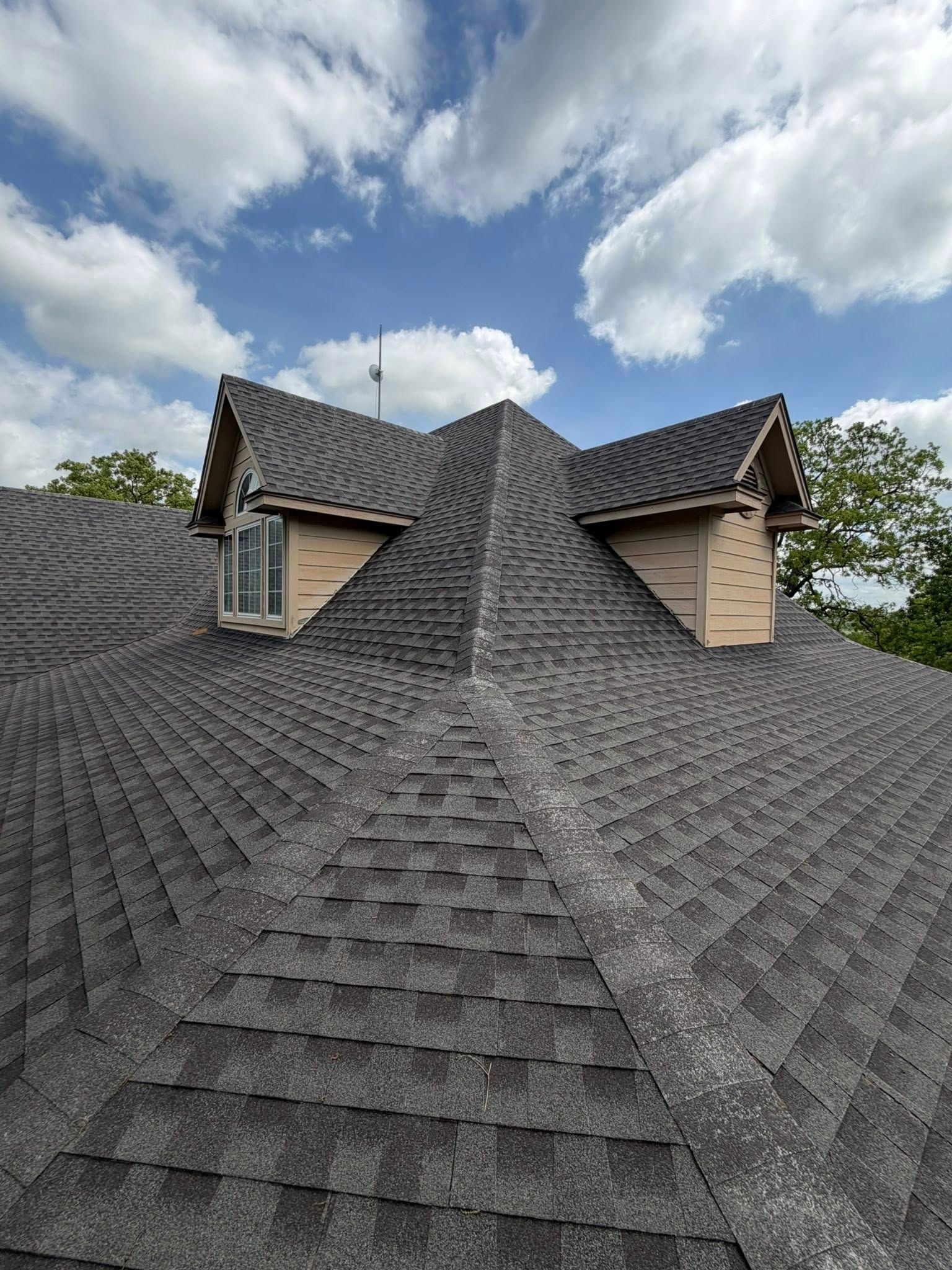 Steep gray shingle roof with dormer windows under a partly cloudy sky