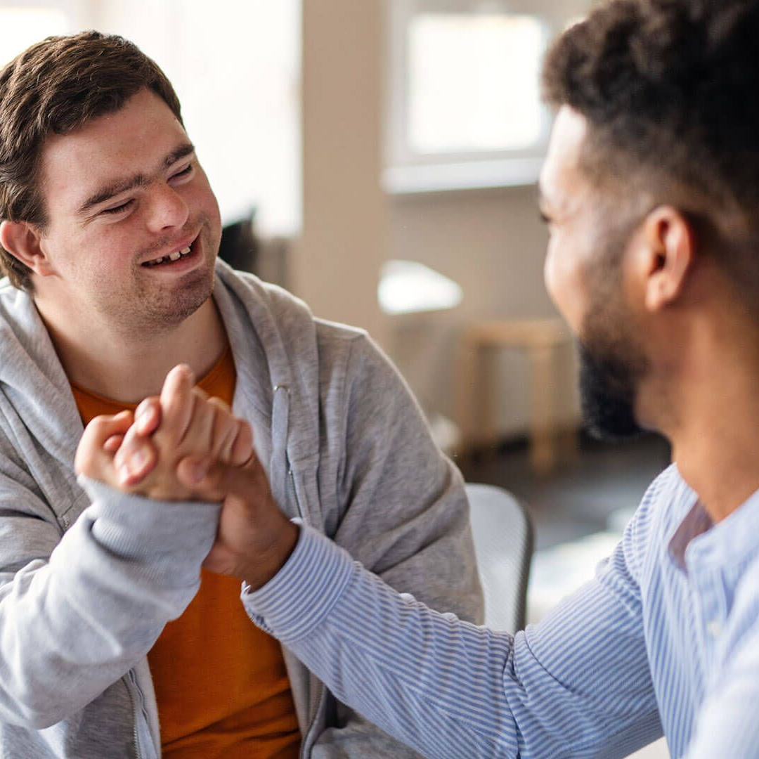 A support worker and a young man with Down syndrome sharing a handshake