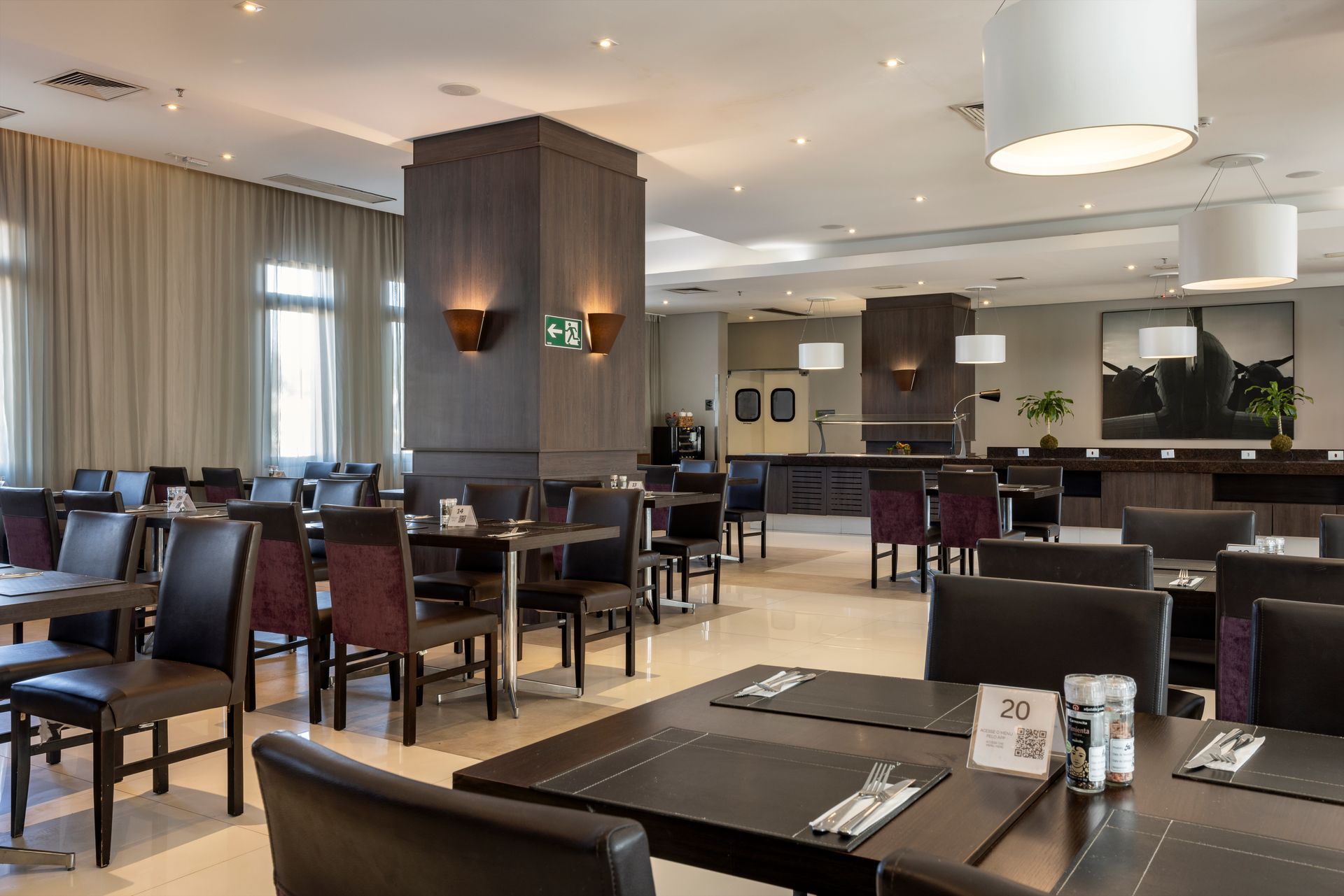Sala de jantar moderna de restaurante com mesas postas, cadeiras escuras e iluminação aconchegante.