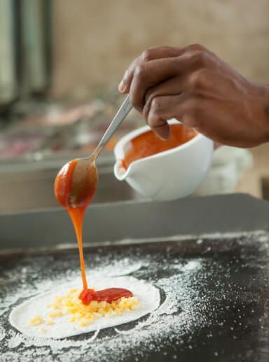 Despejando molho de laranja manualmente de uma tigela branca sobre uma sobremesa em uma assadeira polvilhada com farinha.