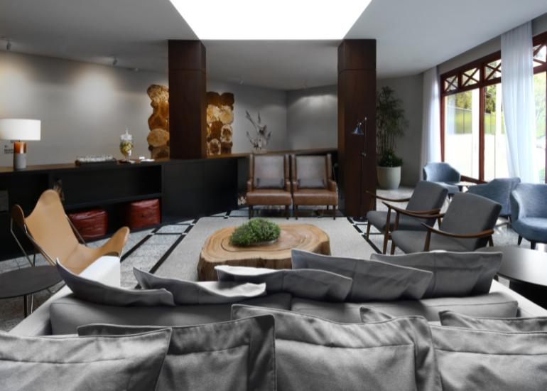 Sala de estar moderna com sofá modular cinza, mesa de centro, detalhes em madeira escura e janelas amplas.