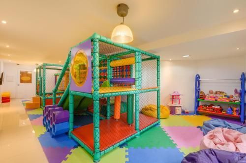 Sala de jogos interna com tapetes de espuma coloridos e uma grande estrutura de escalada verde e roxa.