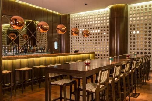 Interior de bar moderno, aconchegante e com iluminação suave, com uma longa mesa de madeira, banquetas e luminárias pendentes de cobre.