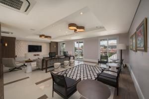 Sala de estar moderna com sofá, cadeiras, TV, mesa de jantar e grandes janelas com vista para uma varanda.
