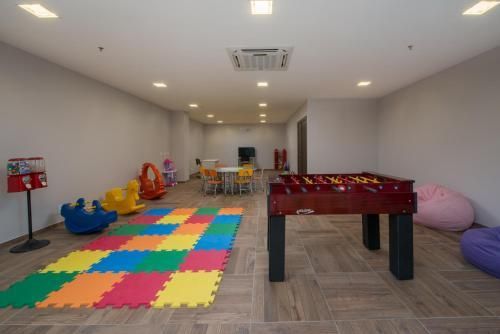 Sala de jogos iluminada com tapetes de espuma no chão, brinquedos, mesa de pebolim e assentos coloridos.