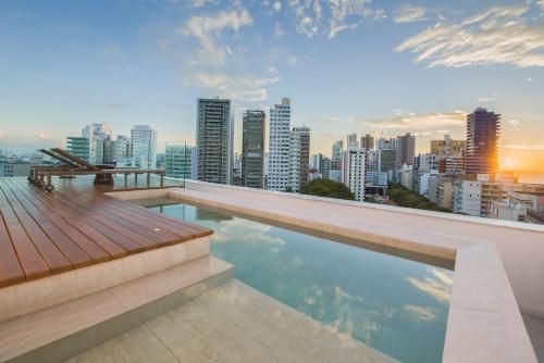 Piscina infinita na cobertura com vista para o horizonte da cidade ao pôr do sol e deck de madeira para relaxar.