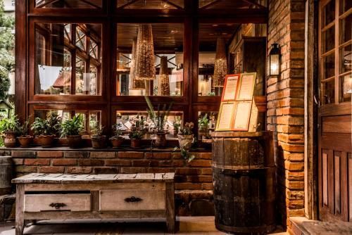 Varanda rústica e aconchegante com janelas de madeira, vasos de plantas e uma lanterna acesa ao lado de um banco.