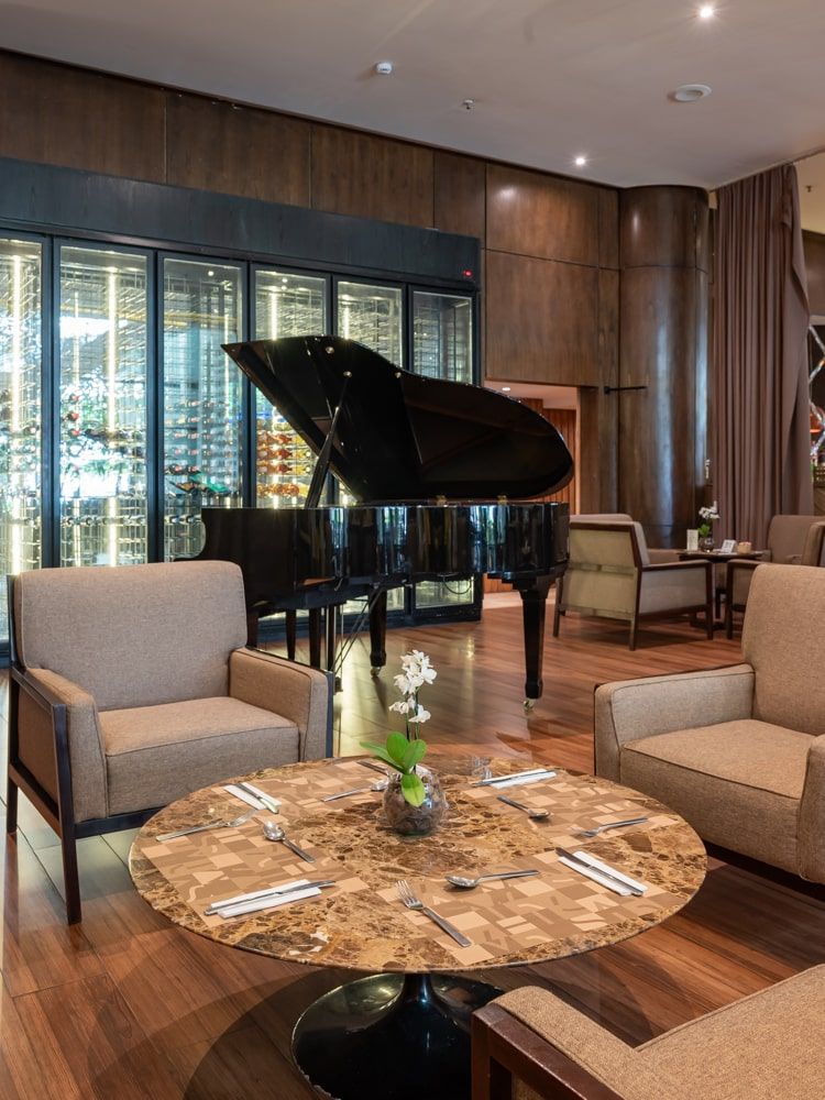 Sala de estar moderna com piano de cauda, ​​cadeiras bege, mesa de mármore e vista para a cidade através de grandes janelas.