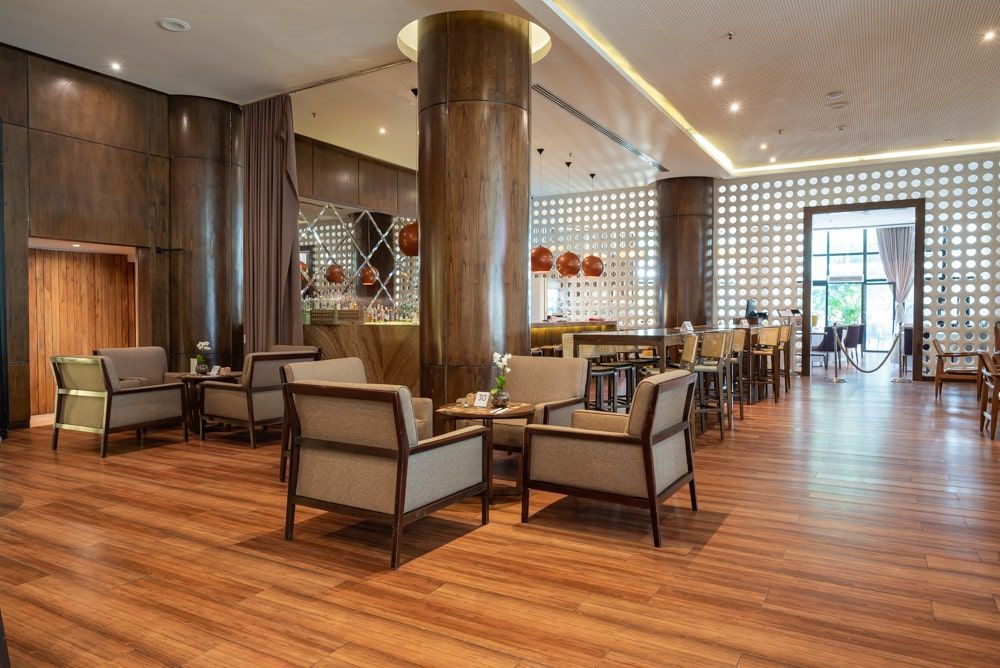 Hall de entrada moderno com piso de madeira, sofás, colunas redondas e área de check-in.