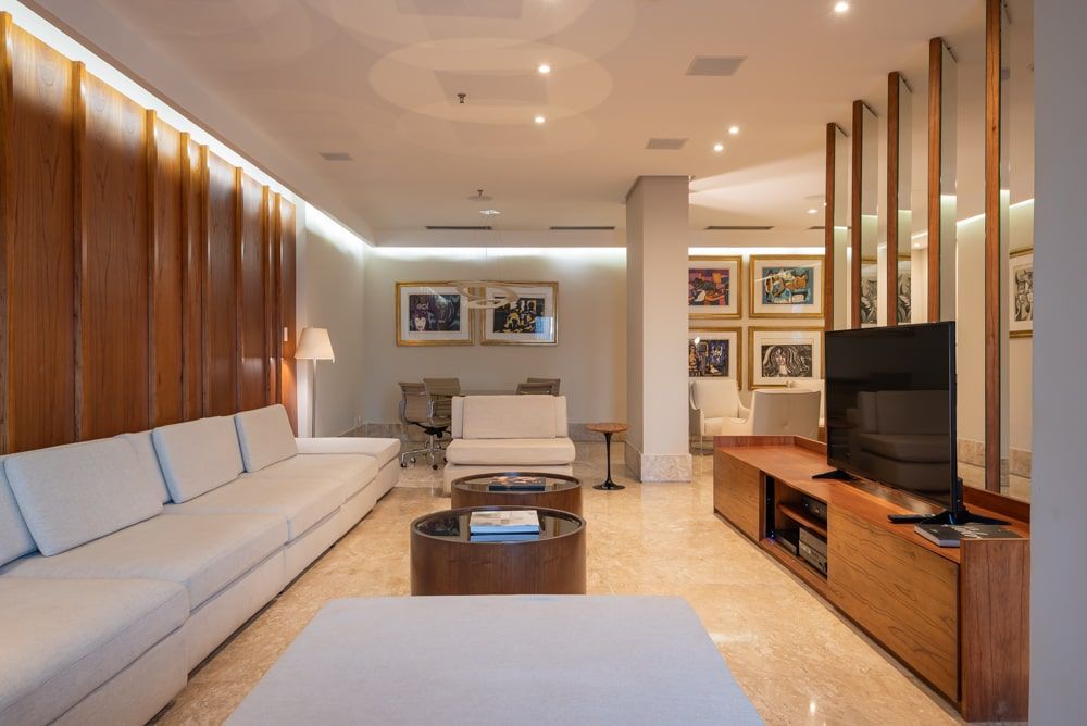 Sala de estar moderna com sofá branco comprido, painéis de madeira na parede, mesa de centro, suporte para TV e obras de arte emolduradas.