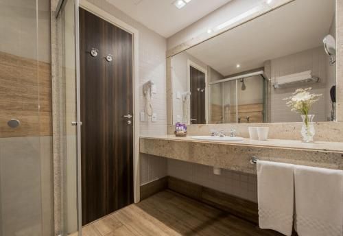 Banheiro moderno com espelho grande, bancada de madeira, box de vidro e azulejos bege.