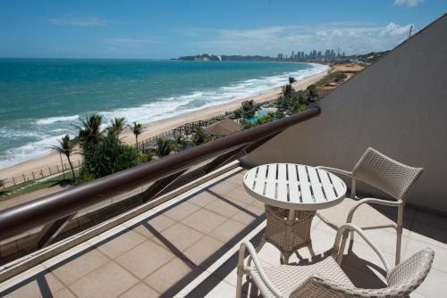 Varanda com mesa e cadeiras com vista para uma praia ensolarada e o oceano.