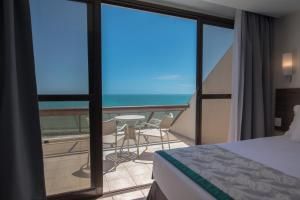 Quarto de hotel com portas de vidro deslizantes que dão para uma varanda com vista para o mar.