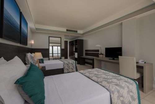 Quarto de hotel moderno com duas camas, TV, escrivaninha e janelas amplas.