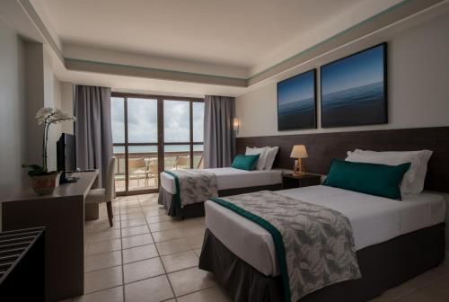 Quarto de hotel moderno com duas camas, detalhes em azul-turquesa, portas para varanda e vista para o mar.