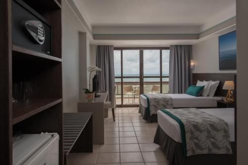 Quarto de hotel moderno com duas camas, piso de azulejo e portas de varanda com vista para o mar.