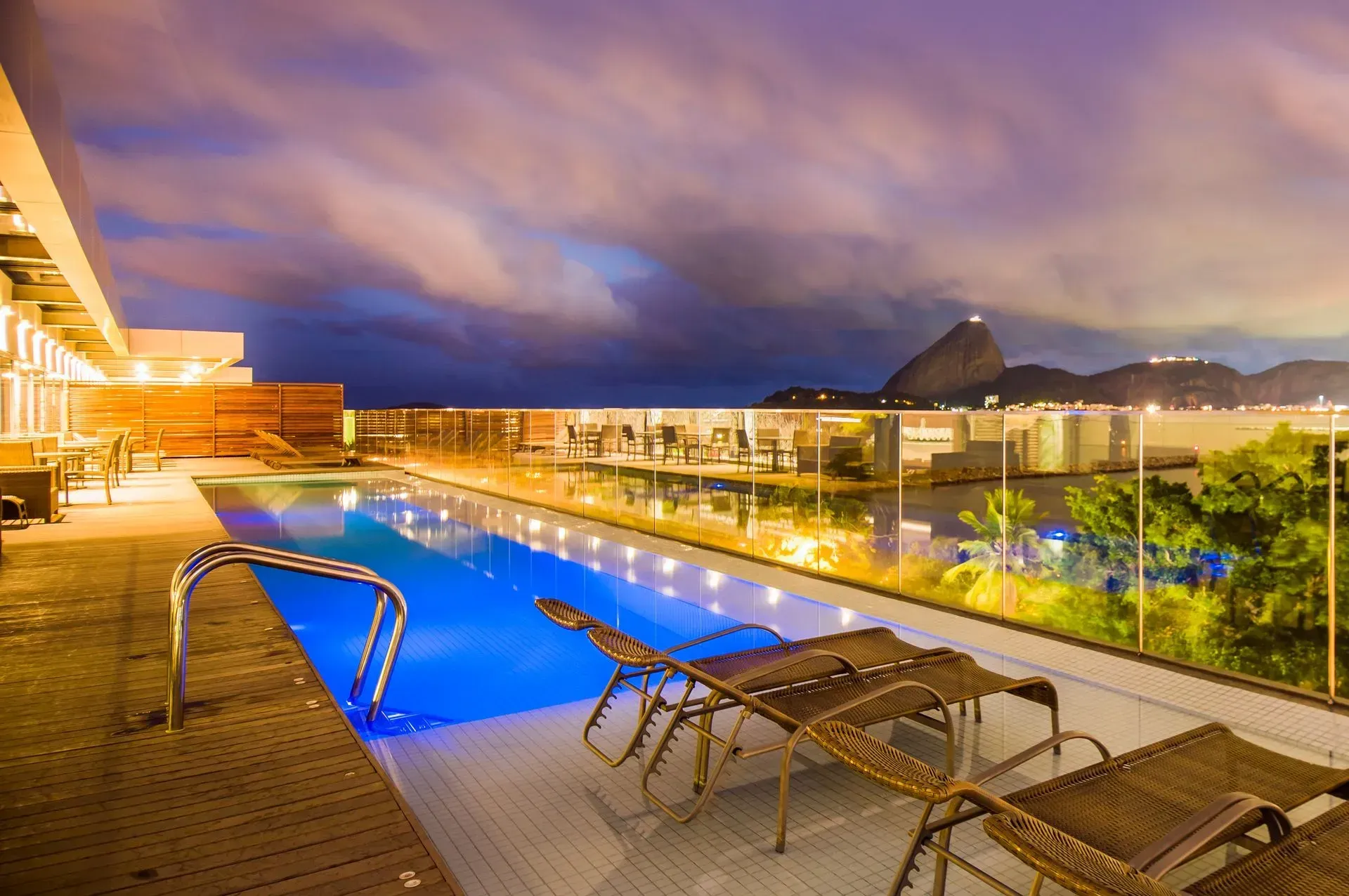 Piscina infinita na cobertura ao entardecer, com espreguiçadeiras, iluminação aconchegante e vista para a montanha.