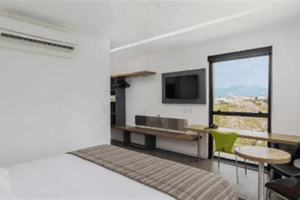 Quarto moderno com cama, escrivaninha, TV de parede e janela ampla com vista para as montanhas.