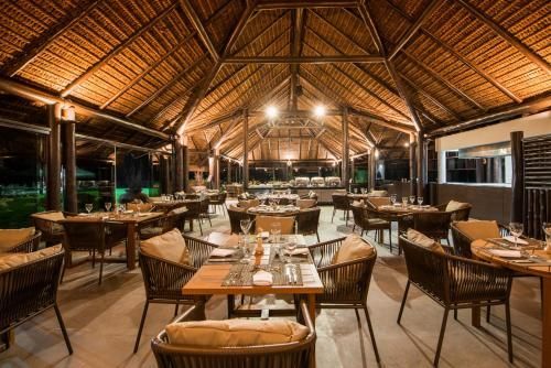 Restaurante ao ar livre com mesas e cadeiras de vime sob um aconchegante teto de palha de madeira.