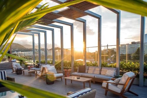 Terraço ensolarado na cobertura com espreguiçadeiras, pérgola e vista da cidade ao pôr do sol.