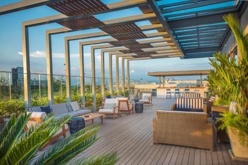 Lounge moderno na cobertura com cadeiras de vime, pérgola e vista da cidade ao pôr do sol.
