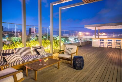 Terraço na cobertura com espreguiçadeiras, almofadas listradas, deck de madeira e luzes da cidade ao entardecer.