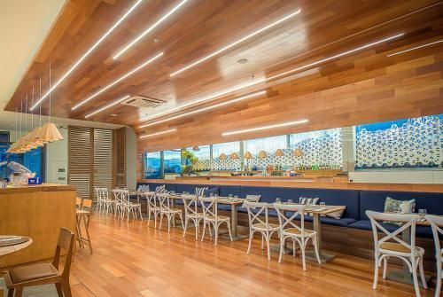 Interior de restaurante moderno com teto de madeira, bancos estofados azuis e mesas e cadeiras brancas.