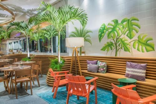 Café colorido com cadeiras laranja, tapete turquesa, banco de madeira e arte tropical nas paredes internas.