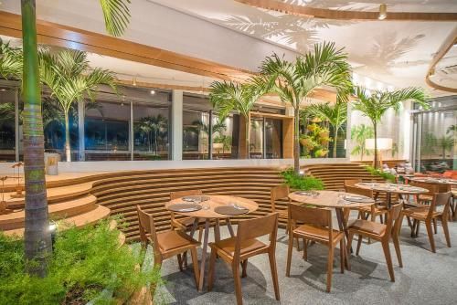 Pátio externo moderno de restaurante com mesas e cadeiras de madeira, palmeiras e iluminação aconchegante.
