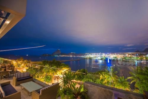 Vista noturna da cidade à beira-mar a partir de um terraço com espreguiçadeiras, palmeiras e edifícios iluminados do outro lado da baía.