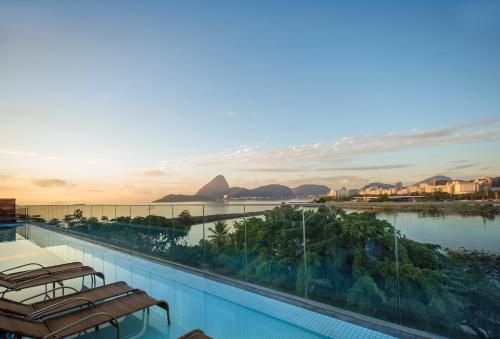 Piscina na cobertura com vista para uma baía tranquila ao pôr do sol, com montanhas ao fundo.