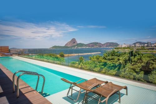 Piscina infinita com vista para uma baía tropical, espreguiçadeiras e uma montanha ao longe.