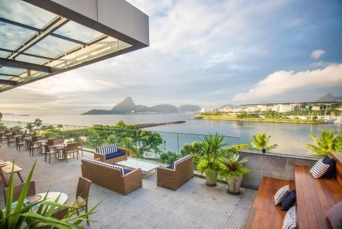 Terraço luxuoso com espreguiçadeiras com vista para uma baía tranquila e montanhas ao longe ao pôr do sol.