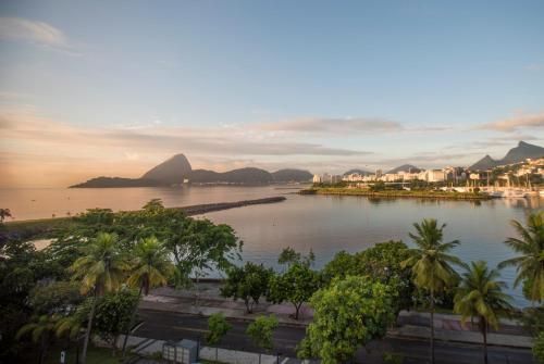 Pôr do sol sobre uma baía tranquila com palmeiras, montanhas ao longe e edifícios à beira-mar.
