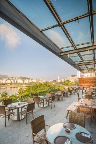 Terraço de restaurante na cobertura com mesas, cadeiras e vista para o horizonte da cidade sob uma cobertura de vidro.
