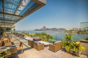 Terraço ensolarado com cadeiras de vime, palmeiras em vasos e vista para o oceano e para a montanha sob um toldo de vidro.