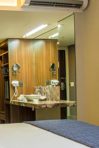 Quarto de hotel com espelho de maquilhagem, luzes de parede e uma cama em primeiro plano.