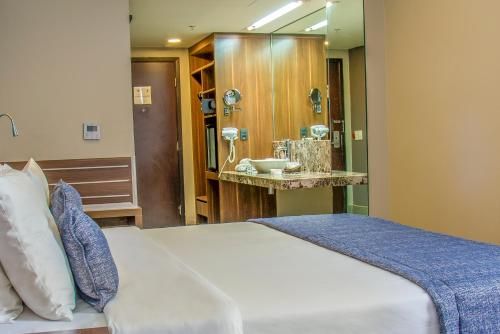 Quarto de hospital com cama arrumada e pia com armários de madeira e espelho.