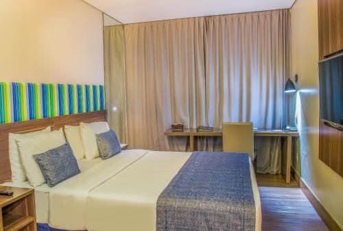 Quarto de hotel moderno com duas camas de solteiro, detalhes em azul, escrivaninha e cortinas do chão ao teto.