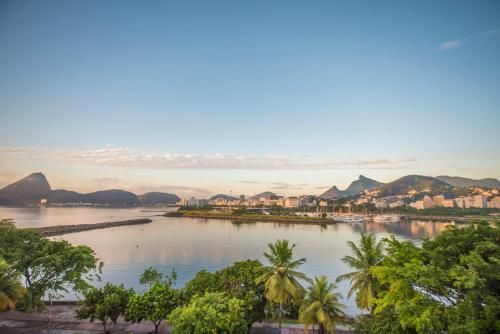 Baía costeira com águas calmas, palmeiras e montanhas sob um céu azul brilhante ao nascer do sol.
