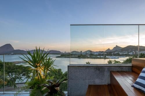 Terraço moderno com guarda-corpo de vidro com vista para uma baía tranquila ao pôr do sol, com montanhas ao fundo.