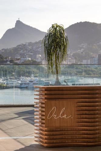Bancada de madeira com vaso de plantas, com vista para a marina e a baía montanhosa ao pôr do sol.