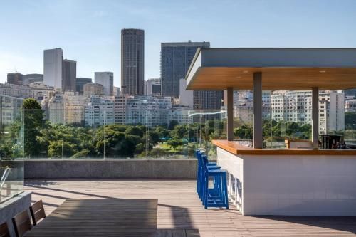 Terraço na cobertura com deck de madeira, cadeiras azuis e vista para o horizonte da cidade além de uma parede de concreto.