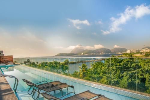 Piscina infinita com vista para colinas verdejantes e uma baía tranquila sob um céu luminoso.