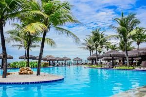 Piscina de resort tropical com palmeiras, água azul e cabanas de palha sob um céu claro.