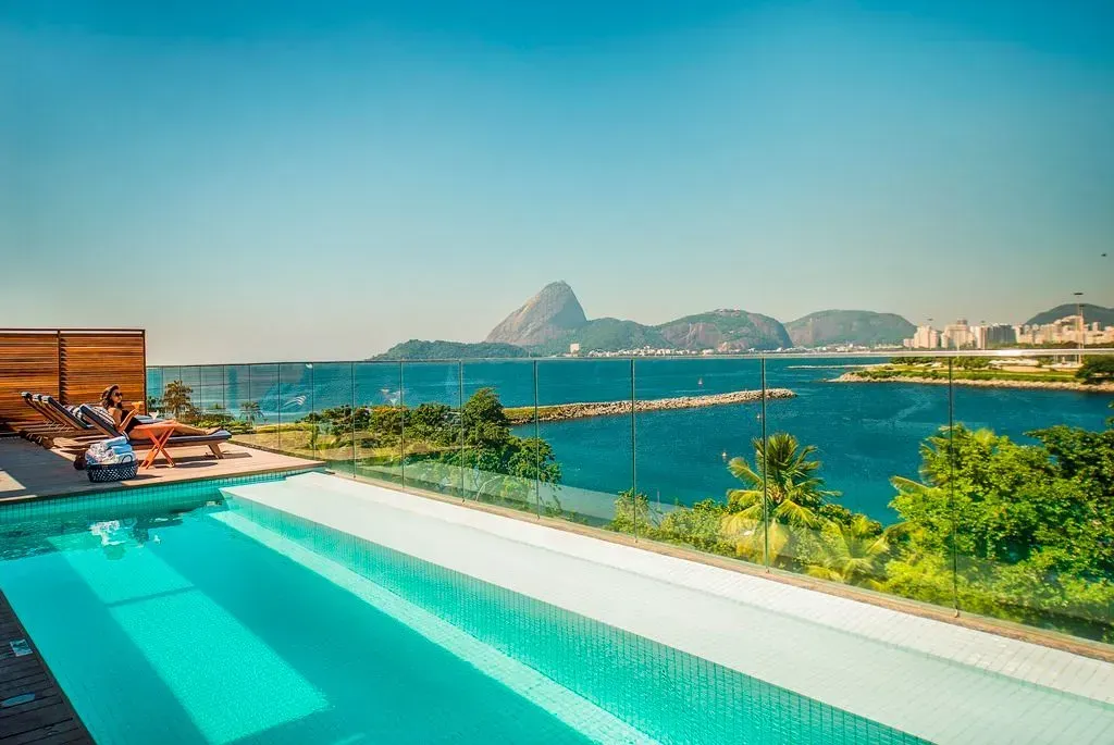 Piscina infinita turquesa com vista para uma baía azul brilhante e montanhas ao longe em um resort de luxo.