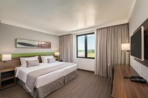 Quarto de hotel moderno com cama grande, TV e janela com cortinas e vista para a cidade.