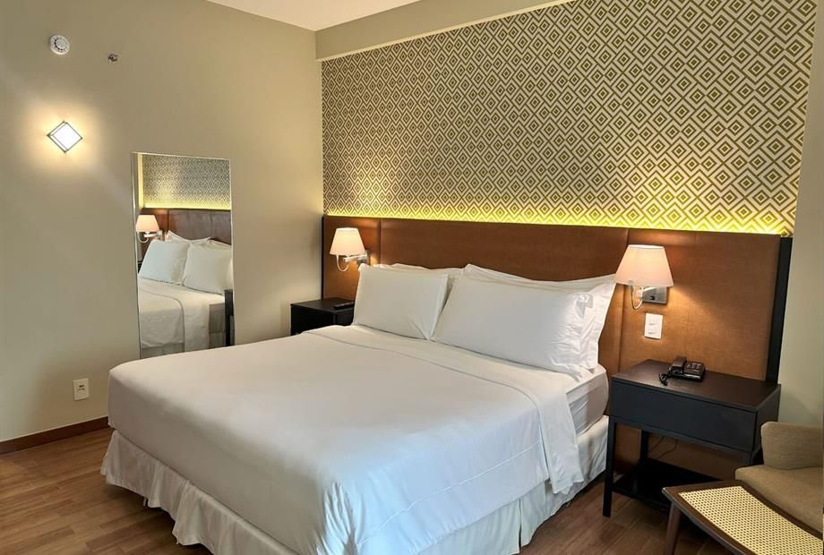 Quarto de hotel moderno com uma cama king-size impecavelmente arrumada, abajures e parede com estampa decorativa.
